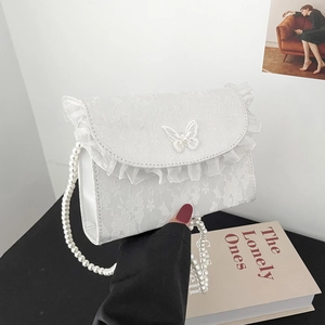 Close-up of white lace shoulder bag featuring organza frills and a pearl chain strap