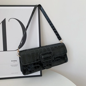 Macro detail of black crocodile embossed patent leather on a baguette shoulder bag