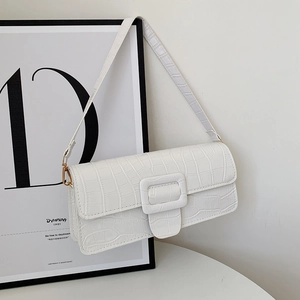 Detail of white crocodile embossed texture and golden hardware on a shoulder baguette bag