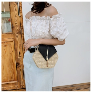 Close-up of hexagonal straw crossbody bag with black leather flap and gold tassel detail