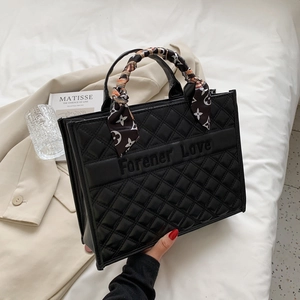 Détail du sac cabas noir matelassé avec logo embossé et poignée ornée d'un foulard en soie
