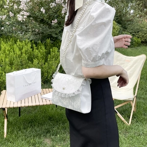 Detail of white lace crossbody bag featuring ruffled edges and a luxury pearl strap