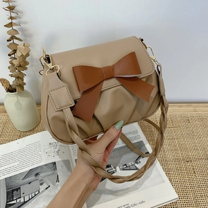 Détail du sac beige plissé avec grand nœud marron et bandoulière en cuir tressé