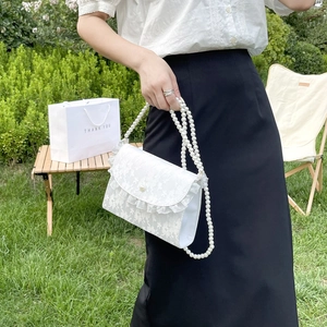 White lace crossbody bag with pearl strap and ruffle edge shown in a hand-held view