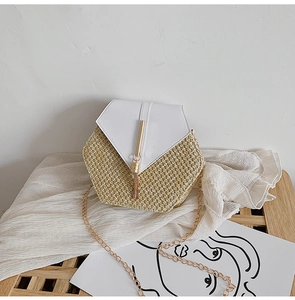 Detail of hexagonal straw crossbody bag with golden tassel and chain on white linen background