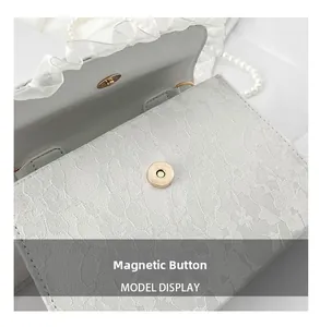 Detail of the magnetic buckle closure on a white lace crossbody bag with ruffles