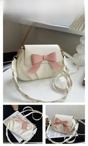 Détail du sac crème avec un grand nœud rose et une bandoulière en maille torsadée chic