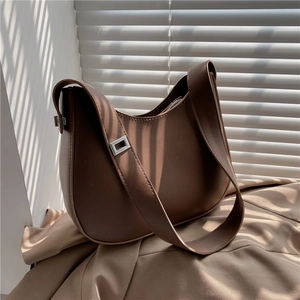 Close-up of a dark brown crescent baguette bag with silver buckles and a wide strap