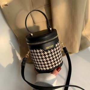 Detail of cylindrical bucket bag in black faux leather and houndstooth fabric with gold zipper