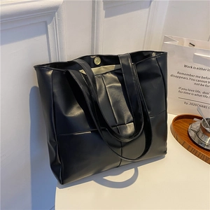 Detail view of black quilted tote bag with gold magnetic clasp on a minimal white tray