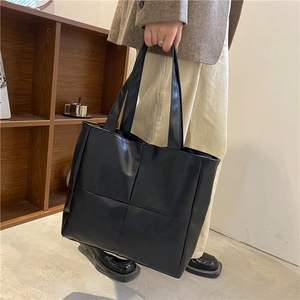 Detail of black large capacity quilted faux leather tote bag with woven design texture