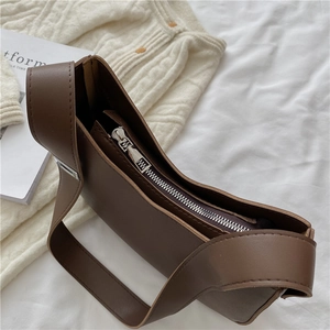 Detail view of silver metal zipper and wide leather strap on dark brown baguette bag