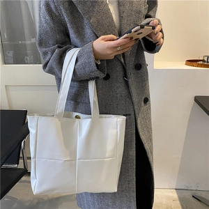 White quilted tote bag with large square pattern shown on shoulder of model in grey coat