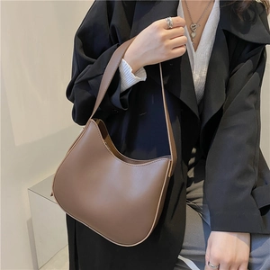 Minimalist brown matte leather half-moon baguette bag worn over the shoulder