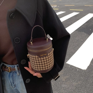 Close-up of houndstooth cylinder bucket bag with leather accents and metal zipper