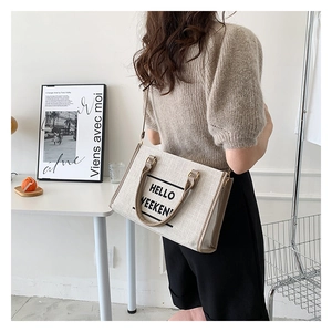Detail of canvas tote bag with 'HELLO WEEKEND' print and contrasting brown trim handles