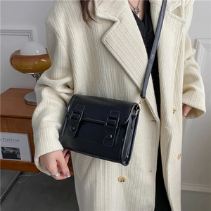 Sacoche classique en cuir noir à double boucle porté sur un manteau en laine beige