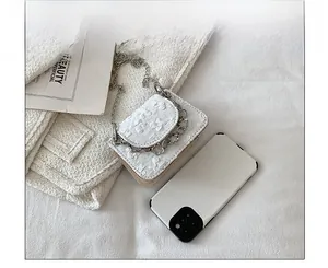 Mini white crossbody bag with floral texture and silver chain next to a smartphone