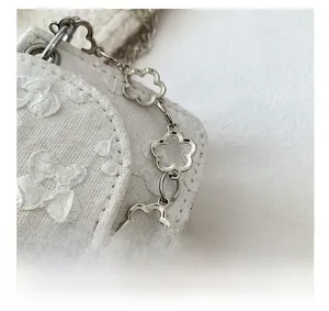 Detailed close-up of white embossed floral texture and silver flower chain on handbag