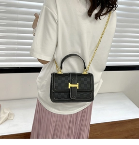 Detail of checkered shoulder bag with golden H-clasp and metal chain strap shown on model