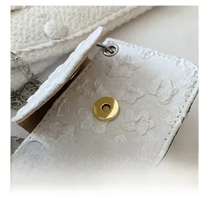 Detail showing the strong magnetic closure and textured jacquard fabric of the white bag