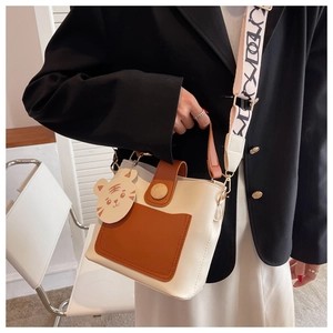 Detail of color-block bucket bag with cartoon tiger charm and jacquard wide shoulder strap