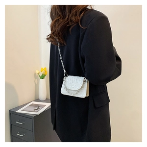 White mini chain crossbody bag with embossed floral texture on model in minimalist setting