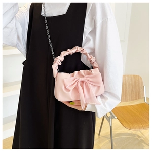 Side view of pink crossbody bag with large bow and ruched handle on a wooden chair