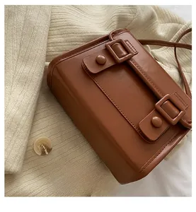 Détail d'un sac bandoulière en cuir marron avec doubles boucles sur fond de pull en maille