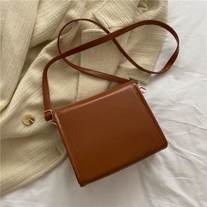 Détail latéral du sac bandoulière marron montrant les coutures et la boucle dorée