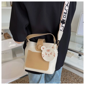 Detail of contrast color bucket bag featuring a tiger charm and wide geometric strap