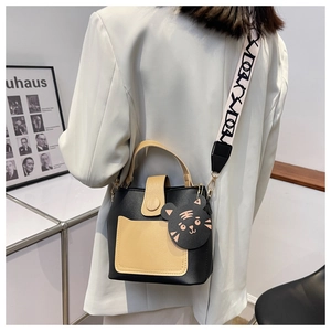 Detail of contrast color bucket bag featuring a wide geometric strap and cartoon charm