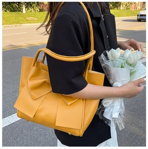 Détail d'un sac cabas jaune vif orné d'un gros nœud, présenté lors d'une séance photo de rue