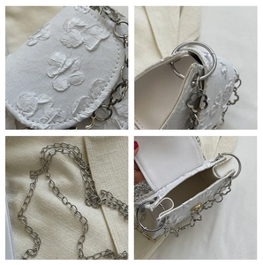 Close-up of 3D butterfly embroidery details and silver chain on a white jacquard bag