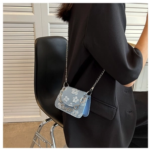 Detail of light blue jacquard mini bag with flower patterns and heart chain on a model