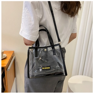 Detail view of transparent PVC tote bag with black glossy straps and inner lettered pouch
