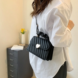 Quilted black crossbody bag with gold heart buckle and ruched handle on a model