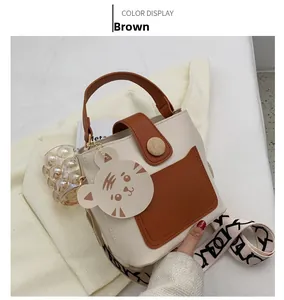 Detail of a brown bucket bag featuring a wide patterned strap and a cute tiger charm