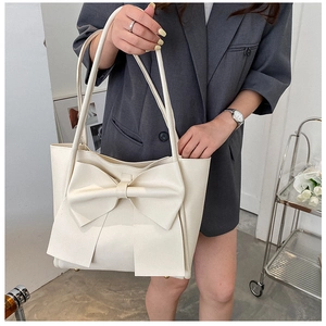 Vue détaillée du grand sac cabas crème avec gros nœud porté à l'épaule par le mannequin