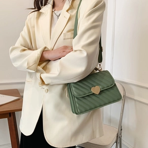 Quilted green crossbody bag with heart lock on woman wearing light blazer