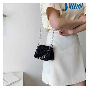 Detail of a black mini chain crossbody bag with 3D floral texture worn by a model