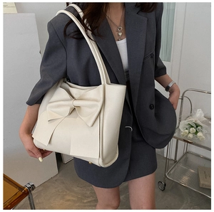 Détail d'un sac cabas crème avec un grand nœud décoratif et des clous de fond en métal