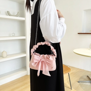Pink crossbody bag with large bow and ruffled handle shown on model in modern room