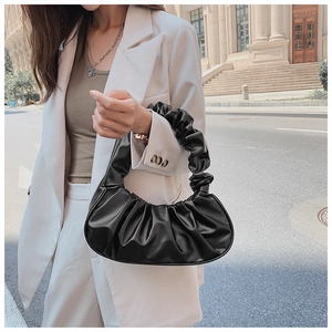 Detail van een zwarte geplooide cloud-tas op een witte blazer voor moderne streetstyle