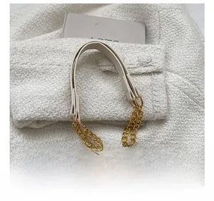 Détail d'une large bandoulière en cuir crème avec une chaîne dorée sur un sac cabas