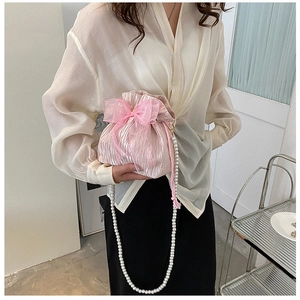 Close-up of pink pleated satin bucket bag with organza bow and long pearl chain strap