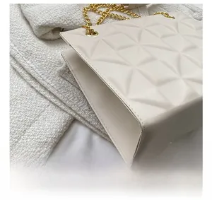 Détail du sac beige avec gaufrage géométrique et bandoulière en chaîne dorée élégante