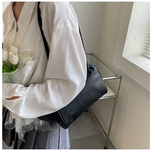 Close-up of minimalist black leather cylinder shoulder bag styled with white tulips