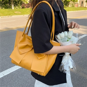 Grand sac fourre-tout jaune avec nœud et pieds en métal dans un décor de rue extérieur