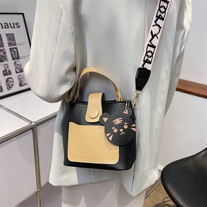 Minimalist color-block bucket bag with wide woven strap and cat charm crossbody view